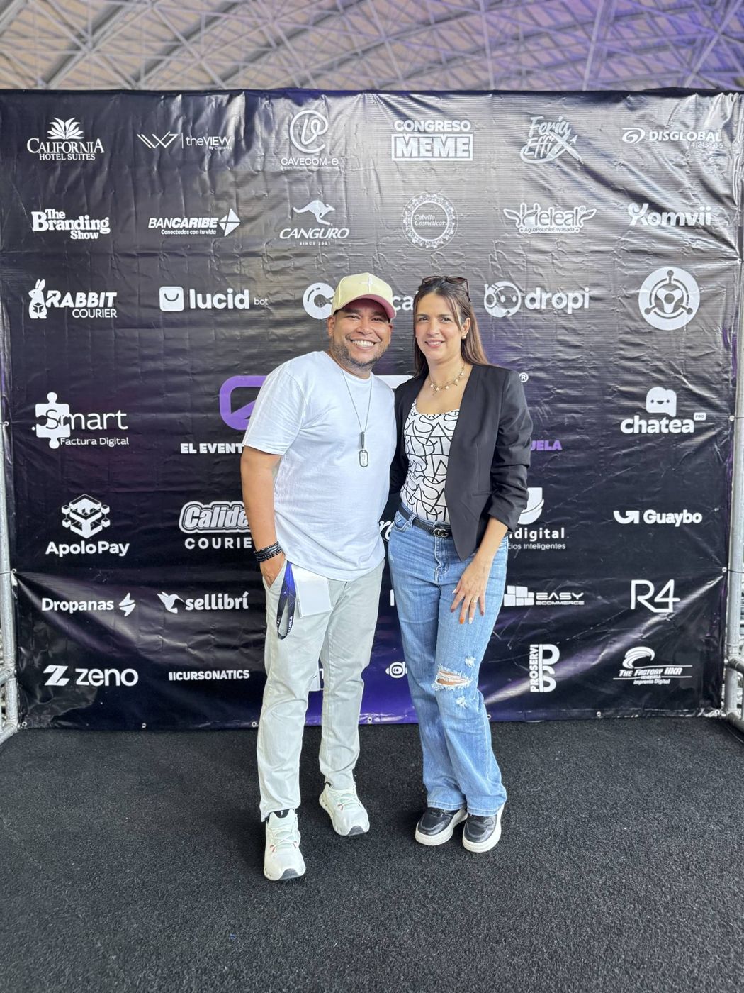 Juan Balza con una asistente frente al backdrop de patrocinantes de eCom Venezuela